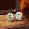 Detailed macro shot of oval green gemstone earrings with double halo in a wooden box - Natural Peridot Stud Earrings