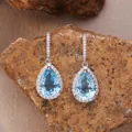 Close-up of pear-shaped blue topaz earrings with halo diamonds on a natural rock background. - Natural Topaz Earrings