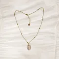 Detalle de un collar de acero dorado con colgante de caracola sobre tela de seda blanca. - Estilo Concha Dorado (YN-1053-C-G)
