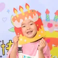 Happy young girl wearing a creative cake-shaped birthday party paper mask for photo props - Orange Cake