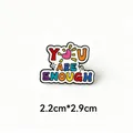 Macro view of colorful 'YOU ARE ENOUGH' enamel pin badge showing exact 2.2cm x 2.9cm size info - You Are Enough