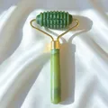 Macro detail of textured green jade facial roller with golden frame on white satin background - Figure 25 (Green Single-Headed Textured Massage Roller)