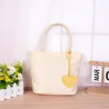Minimalist cream-colored tote bag featuring a yellow heart charm and dual handles - Beige