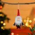 Adorable Christmas gnome fabric ornament hanging on a twig with festive bokeh lights. - Red Hat Green Body Santa