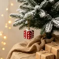 Red gift box Christmas tree ornament with white dots hanging on snow-covered pine branch - Gift Box Pendant