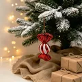Rot-weiß gestreifter Zuckerstangen-Weihnachtsbaumschmuck an einem verschneiten Zweig - Süßigkeiten Anhänger