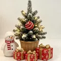 Kleiner schneebedeckter Weihnachtsbaum im Korb mit roter Kugel und warmer Lichterkette - Rote Kugel mit Perlenanhänger