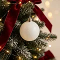 Eleganter weißer glitzernder Weihnachtskugel-Anhänger an einem verschneiten Baum - Weiße Glitzerkugel Anhänger