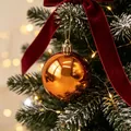 Festliche kupferfarbene Weihnachtskugel an einem verschneiten Tannenbaumzweig. - Bronze Kugel Anhänger