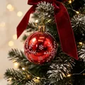 Rote Weihnachtskugel mit weißen Schneeflockenmustern an einem verschneiten Baum - Rote Kugel mit weißen Schneeflocken