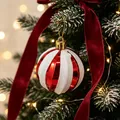 Festliche rot-weiß gestreifte Glitzer-Weihnachtskugel, die an einem Tannenbaum hängt. - Rot und weiß gestreifte Kugel