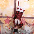 Buffalo plaid Christmas stocking featuring a cute hanging gnome in a festive setting - Red