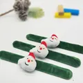 Nahaufnahme von drei grünen Plüsch-Weihnachtsmann-Klapparmbändern auf hellgrauem Grund - Weihnachtsmann