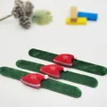 Close-up of green plush slap bracelets featuring decorative red Santa hats for kids. - Hat