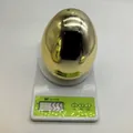Detail view showing a shiny golden plastic Easter egg weighing 55.5g on a scale - 15cm / Approx 55.5g