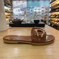 Detailopname van een bruine laksandalen met platte zool en een stijlvolle gouden gesp - Bruin