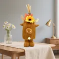 Autumn harvest themed plush highland cow ornament with sunflower and bell on a table - Wearing Hat Style