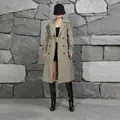 Full body view of a khaki British style trench coat on a model against a stone wall. - XS / Gray