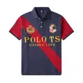 Detailed close-up of a men's navy and red patchwork polo shirt with crest embroidery - 3XL / Tops / Royal Blue Red Contrast