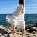 Elegant white high-waisted tiered fringe skirt showing flowing movement by the seaside rocks - M / White