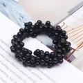 Close-up detail of a black beaded hair scrunchie on a lifestyle magazine background - Black