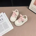 Close-up view of white kids' sneakers featuring sparkly star detail and pink laces. - 26 / Rice Pink