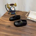 Klassische schwarze Retro-Mary-Jane-Lederschuhe für Mädchen auf einem Vintage-Holztisch - Schwarz