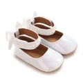 Primer plano de zapatos de bebé blancos brillantes con correas de perlas y lazos traseros - Blanco