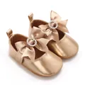 Close-up of champagne gold baby Mary Jane shoes with bow and rhinestone detail - Gold