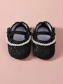 Detailaufnahme der schwarzen Baby-Prinzessinnenschuhe mit eleganten Kunstperlen und Schleifen. - Schwarz