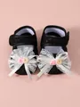 Close-up detail showing the intricate white lace bow and roses on black baby shoes - Black