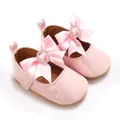 Nahaufnahme von rosa Lackleder-Babyschuhen mit großen Satinschleifen und Strasssteinen. - Rosa