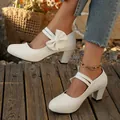 Zapatos elegantes blancos de tacón grueso con lazo y tira Mary Jane sobre suelo de madera - Blanco