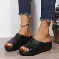 Close-up of black peep-toe platform wedge slides worn with denim jeans. - Black