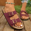 Close-up detail of burgundy suede double buckle slide sandals on a wooden deck background - Burgundy