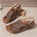 Nahaufnahme brauner Römersandalen mit Keilabsatz und Klettverschluss auf gewebter Matte - Dunkelbraun