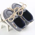 Primo piano di scarpe in tela per neonati grigie con suole morbide e lacci marroni - Grigio