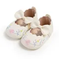 Detail view of cream baby shoes with floral embroidery and a large decorative bow - White