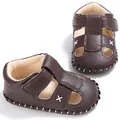 Nahaufnahme von braunen Baby-Sandalen aus Leder mit weißen dekorativen Kreuzstichen - Braun