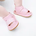 Close-up detail of pink soft-soled infant walker sandals with white lettered straps. - 11cm / Pink