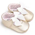Detalle de zapatos dorados de princesa para bebé con elegantes lazos blancos grandes - Dorado