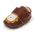Detail van bruine kunstlederen babyschoen met een schattig cartoon leeuwenontwerp. - Bruin