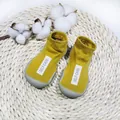 Close-up detail of yellow knit baby sock shoes with grey soft soles resting on a woven straw mat - Size 24/25 (Insole 14.5cm) / Yellow Cloth Tag