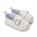Close-up of white soft-soled baby walking shoes with an elegant gold buckle decoration. - White
