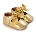 Detaillierte Nahaufnahme von glänzenden goldenen Baby-Prinzessinnen-Schuhen mit großen Schleifen - Gold