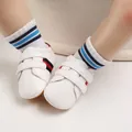 Close-up view of white infant soft sole walking shoes with red and navy blue stripes details - White