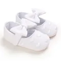 Dettaglio di scarpine bianche da principessa per neonata con ricami a cuore e fiocchi. - Bianco