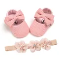 Close-up detail of soft pink knitted baby shoes with matching floral headband set - Pink