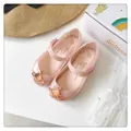 Primer plano de sandalias de gelatina rosa con un emblema metálico de Saturno en oro rosa. - Nude