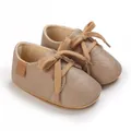 Close-up of beige faux leather baby walking shoes with soft rubber soles and laces. - Camel